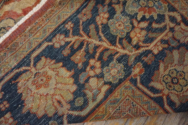 Close-up of a low pile rug displaying a dense traditional pattern in navy, rust, gold, and green tones.