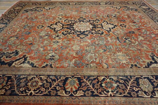 Faded traditional rug featuring a large navy and cream medallion on a distressed terracotta field, resting on wood flooring.