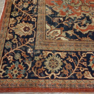 Intricate floral rug corner in navy blue, rust, and tan on weathered wood flooring.