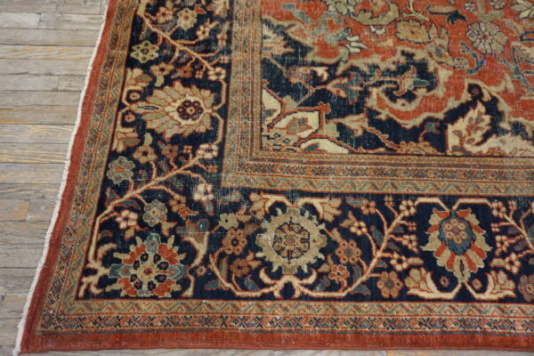 Intricate floral rug corner in navy blue, rust, and tan on weathered wood flooring.