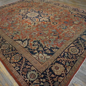 Intricate floral rug with a rust red field and navy border rests on distressed wooden floors.