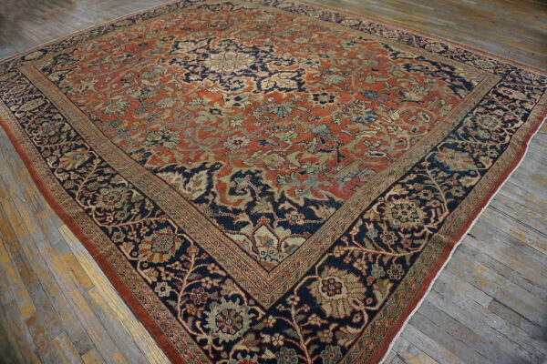 Intricate floral rug with a rust red field and navy border rests on distressed wooden floors.
