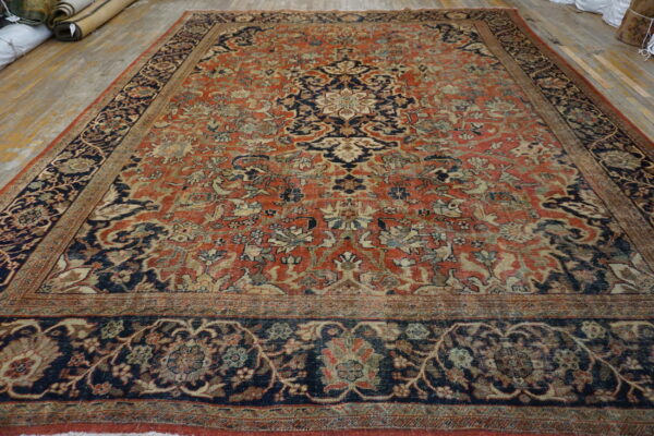 Ornate medallion rug featuring faded terracotta, navy, and cream colors, displayed on light wooden floorboards.