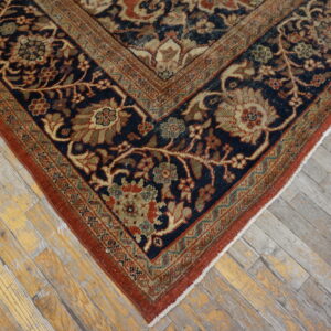 Navy and rust-toned rug featuring a dense floral pattern placed on weathered wood planks.