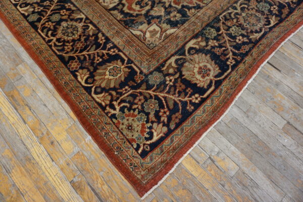 Navy and rust-toned rug featuring a dense floral pattern placed on weathered wood planks.