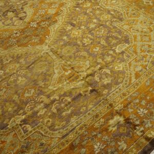 Golden orange, olive green, and brown traditional patterned rug resting on light wood flooring.