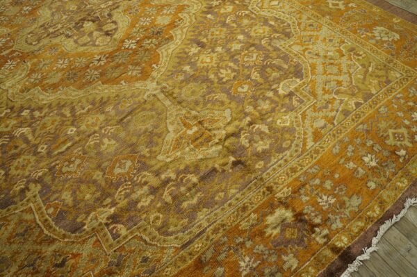 Golden orange, olive green, and brown traditional patterned rug resting on light wood flooring.