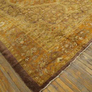 A close-up shows a gold, olive, and brown ornate rug lying on distressed wood floorboards.