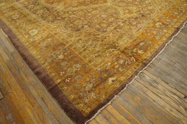 A close-up shows a gold, olive, and brown ornate rug lying on distressed wood floorboards.