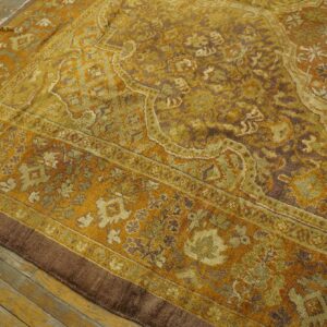 Gold and brown ornate low-pile rug with a complex border laid over distressed wooden flooring.
