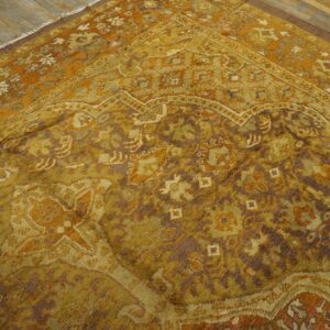 Close view of a traditional low-pile rug in golden orange, olive, and brown on wood planks.