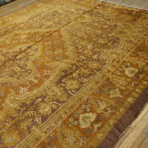 Detailed gold, brown, and green patterned rug with low pile lies on light-colored wooden plank floor.