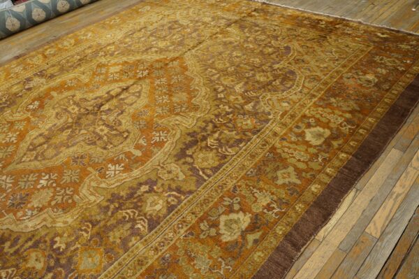 Detailed gold, brown, and green patterned rug with low pile lies on light-colored wooden plank floor.