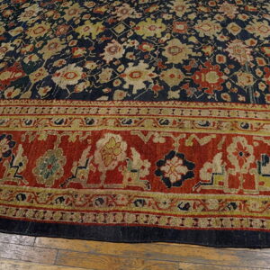 A navy blue floral field contrasts with a wide red and gold border on light brown hardwood flooring.