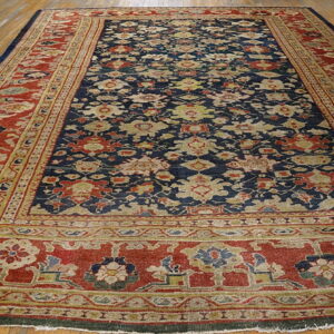 Low-pile navy blue and red rug with an all-over botanical pattern displayed on wooden flooring.