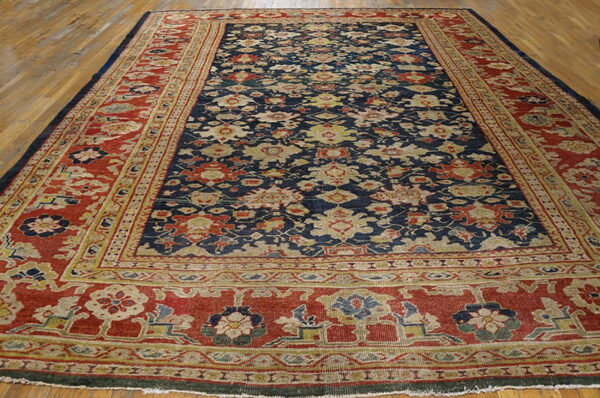 Low-pile navy blue and red rug with an all-over botanical pattern displayed on wooden flooring.