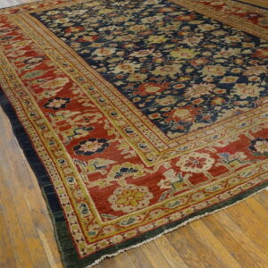 Large navy floral rug with wide red and gold borders rests on light-colored hardwood flooring.