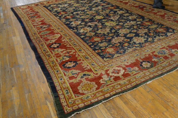 Large navy floral rug with wide red and gold borders rests on light-colored hardwood flooring.