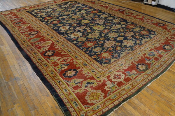 Navy rug with an all-over floral design and a wide red border rests on light wood planks.