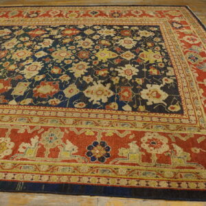 Ornate traditional rug with a navy floral field and wide terracotta border rests on aged wood planks.