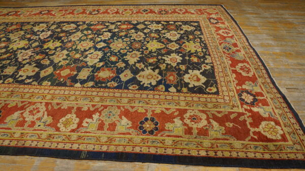 Ornate traditional rug with a navy floral field and wide terracotta border rests on aged wood planks.