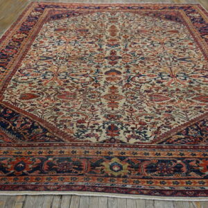 Large traditional low-pile rug with a cream field, red and navy pattern, resting on plank wood flooring.