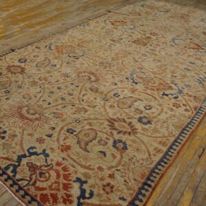 Low-pile tan rug featuring large rust and indigo floral motifs on distressed wood flooring.