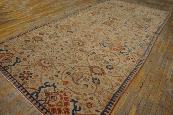 Low-pile tan rug featuring large rust and indigo floral motifs on distressed wood flooring.