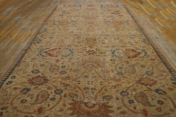Low-pile beige rug with complex traditional rust and blue pattern rests on distressed wooden planks.