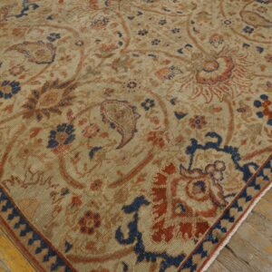 Low-pile beige area rug with ornate navy and rust floral patterns on distressed yellow wood floors.