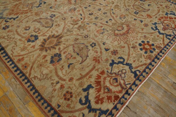 Low-pile beige area rug with ornate navy and rust floral patterns on distressed yellow wood floors.