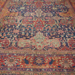 Detailed traditional rug in dark blue, red, and beige, with complex borders on light wood flooring.