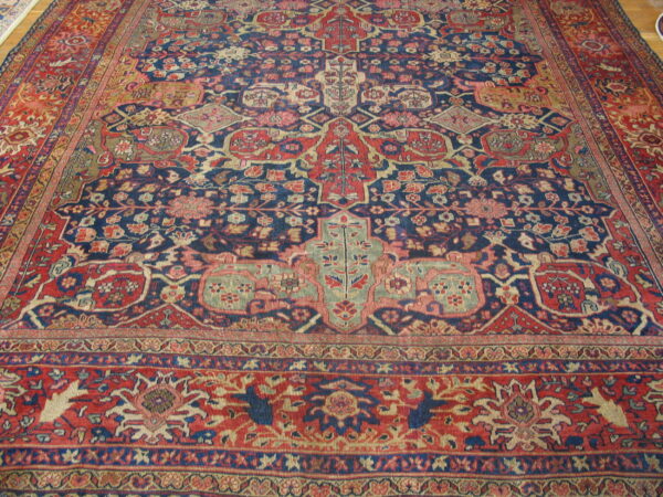 Detailed traditional rug in dark blue, red, and beige, with complex borders on light wood flooring.