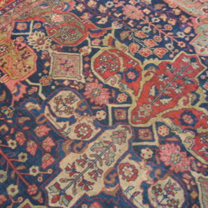 A detailed, traditional rug pattern features geometric designs in navy blue, red, khaki, and light pink.