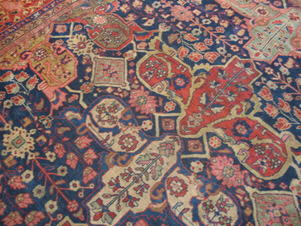 A detailed, traditional rug pattern features geometric designs in navy blue, red, khaki, and light pink.