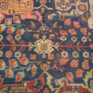Low pile rug showing intricate botanical patterns in red, gold, and pink on a navy blue field.