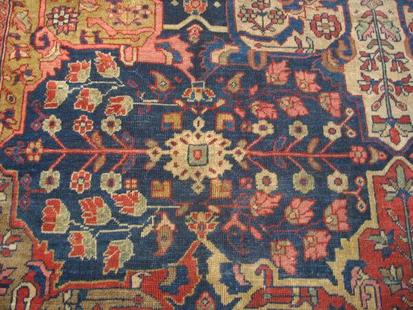 Low pile rug showing intricate botanical patterns in red, gold, and pink on a navy blue field.
