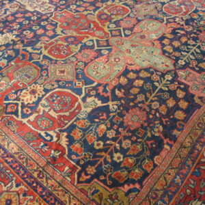 Intricate floral rug pattern in deep blue, red, beige, and muted green shown close-up.