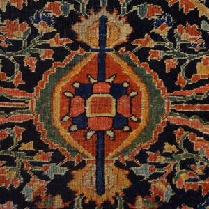 Detailed view of a traditional low-pile rug pattern with a central geometric motif and dense floral design on a navy field.