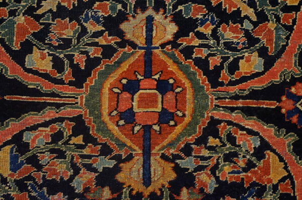 Detailed view of a traditional low-pile rug pattern with a central geometric motif and dense floral design on a navy field.