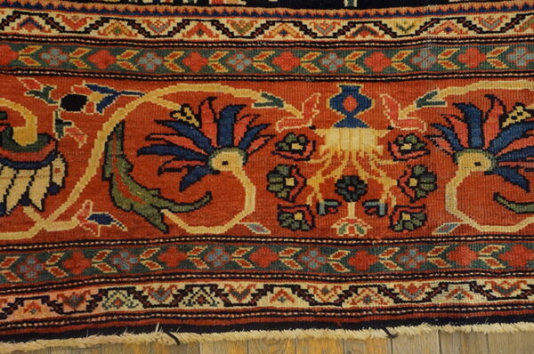 Ornate rug detail featuring a burnt orange field, navy florals, green accents, and intricate patterned borders.