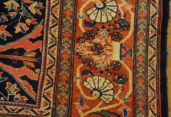 Detailed low-pile rug section in rust, navy, cream, and green with traditional floral and geometric patterns.