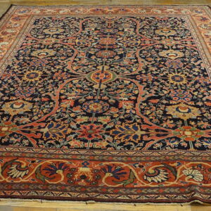 Dark blue rug with dense multicolored floral patterns and broad orange-red borders rests on wood planks.