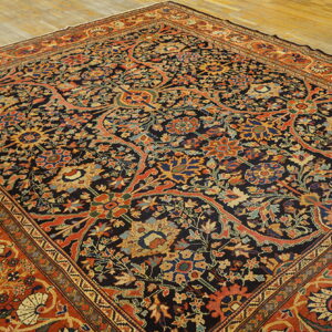 Ornate navy and rust rug featuring complex multicolored floral patterns, displayed on light wooden plank flooring.