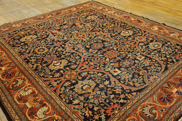 Ornate navy and rust rug featuring complex multicolored floral patterns, displayed on light wooden plank flooring.