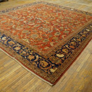 A large rust-colored rug with an intricate floral pattern and a wide navy blue border lies on hardwood floors.