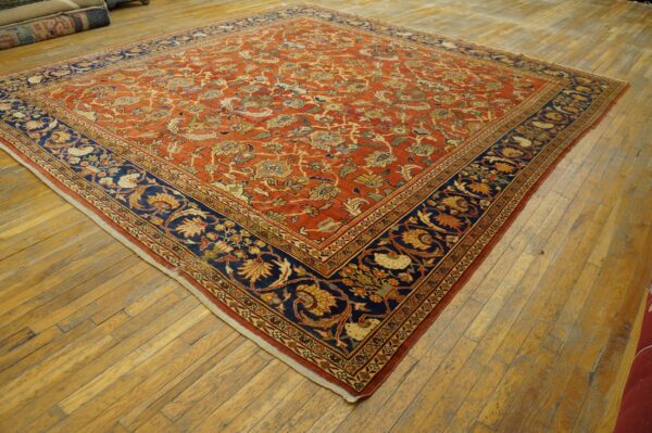 A large rust-colored rug with an intricate floral pattern and a wide navy blue border lies on hardwood floors.