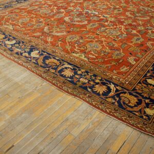 Terracotta floral rug featuring a complex vine pattern and a contrasting dark blue border on distressed wood.