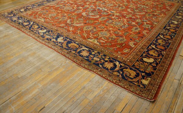 Terracotta floral rug featuring a complex vine pattern and a contrasting dark blue border on distressed wood.