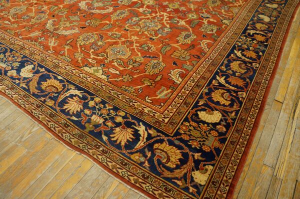 Ornate floral rug with a rust field and a navy border, laid diagonally across distressed wood floors.